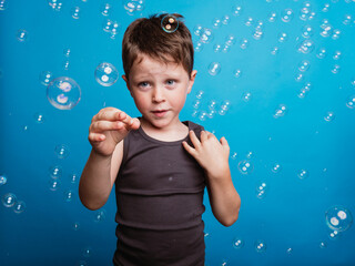 Shocked child showing touching gesture in studio with soap bubbles