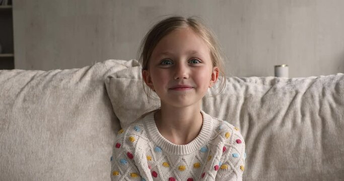 Head shot portrait little girl sit on sofa at home waving hand start video conference remote conversation. Young generation and modern tech usage, online study, videocall event, distant class concept