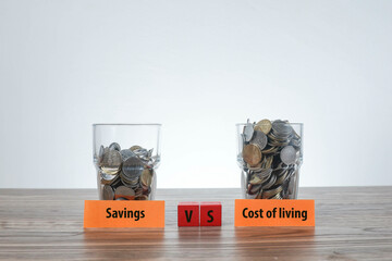 Savings vs Cost of Living was written on the wooden blocks in front of the pile of coins in the...