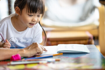 A cute 3-year-old Asian girl is practicing writing and reading. It is an image that focuses on the...
