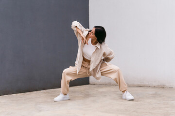 Stylish woman dancing on street near wall