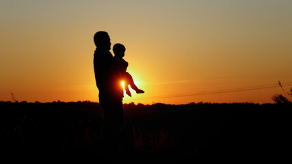 Caring father holds the baby on his arms, unrecognizable silhouette at sunset, paternal love