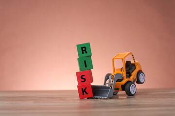 A toy bulldozer lifting wooden blocks written RISK