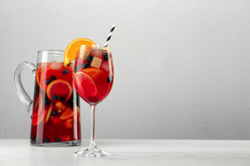 Glass and jug of Red Sangria on white wooden table against light grey background. Space for text
