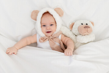 a child in a funny hat with ears with a teddy bear under the blanket. Textiles and bed linen for children. A newborn baby has woken up or is going to bed