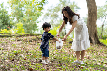 Happy Asian mother and little son are collecting trash into a bag. Mom and little boy volunteer charity environment outdoor in the park