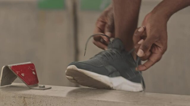 Slowmo close-up of unrecognizable African-American sportsman tying shoelaces on his trainers while jogging outdoors in urban environment