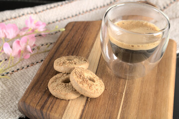 Black coffee in a double-bottomed glass with cookies on wood