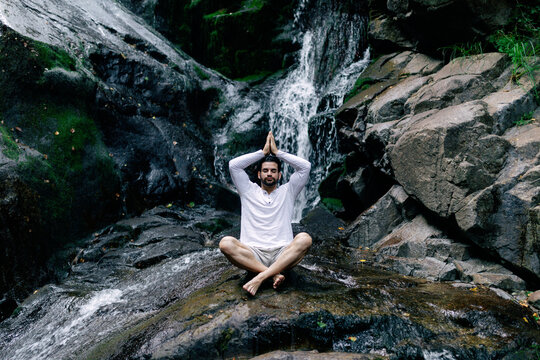 Relaxed man meditating near waterfall