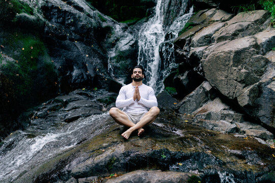 Relaxed man meditating near waterfall