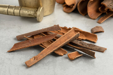 Heap of dried Cinnamon bark close up in front of a traditional mortar and pestle ready to ground  