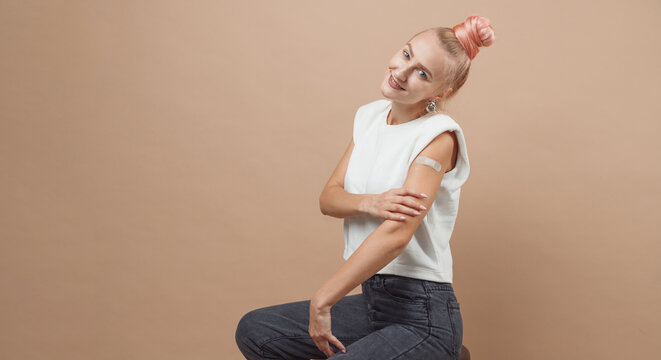 Young hipster woman with band aid after coronavirus Covid-19 vaccine injection. Covid vaccination concept, plain color background