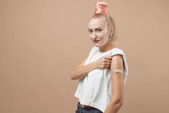 Young hipster woman with band aid after coronavirus Covid-19 vaccine injection. Covid vaccination concept, plain color background