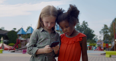 Medium shot of multiracial kids using cellphone at playground
