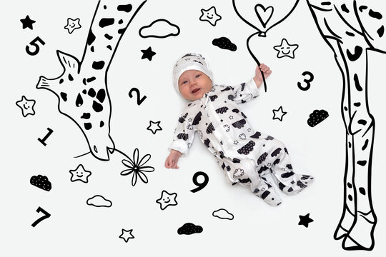Portrait of a child in overall and a hat with a black and white drawing, lying on a rug with a black and white hand drawing image of  a giraffe giving a flower