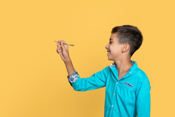 Young boy wearing blue shirt writing on a yellow wall, profile