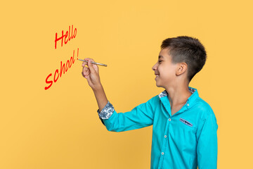 Young boy wearing blue shirt writing on a yellow wall, profile
