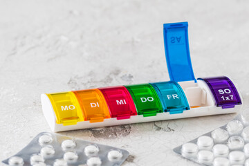 Colorful pill box for weekly dosing on a white background, abbreviations for days of the week in...