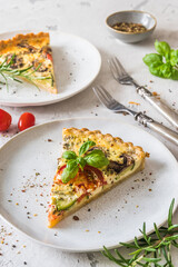 Piece of homemade vegetable tart with mushrooms, tomatoes and zucchini on white background, vertical