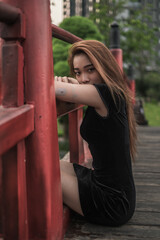 Obraz premium Portrait of beautiful young asian woman in casual black dress sitting in the park and looking at camera with copy space. Lovely Vietnamese girl