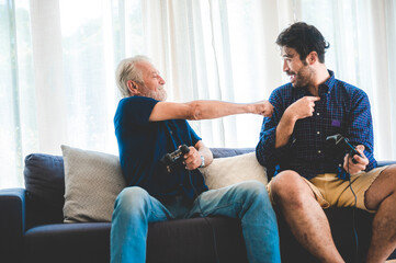 Playful senior father and young son sitting and relaxing on sofa at home playing video games and competing with each other