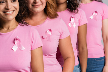 African amercan woman with pink ribbon on t-shirt smiling near friends isolated on grey - Powered by Adobe