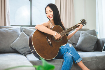 Asian woman playing music by guitar at home, young female guitarist musician lifestyle with acoustic art instrument sitting to play and sing a song making sound in hobby in the house room