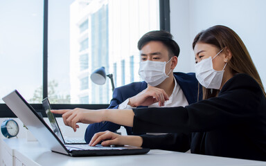 Two asian formal business man and woman wearing face mask to protect virus while working, typing, discussing with confidence and using laptop in the modern office.