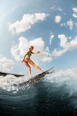 attractive young woman wakesurfer skilfully balancing on surfboard along the river wave