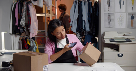 Female warehouse worker holding phone scanning retail package qr-code