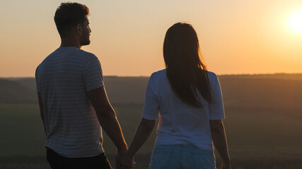 The romantic couple standing on mountain top on sunset background