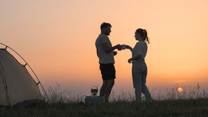 The romantic couple sitting near the campsite tent and preparing tea
