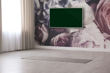 Modern wide screen TV on wall in room with yoga mat