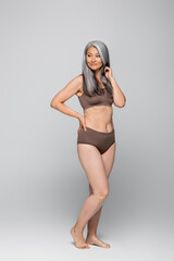 Obraz premium Asian woman in lingerie holding hand on hip on grey background, body positive concept