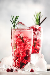 Cranberry cocktail with vodka, ice, juice, rosemary and red berries in highball glass. Refreshing long drink. Gray table background with negative space