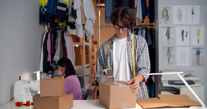 Man seller working in clothing shop warehouse packing clothes preparing parcel for shipping