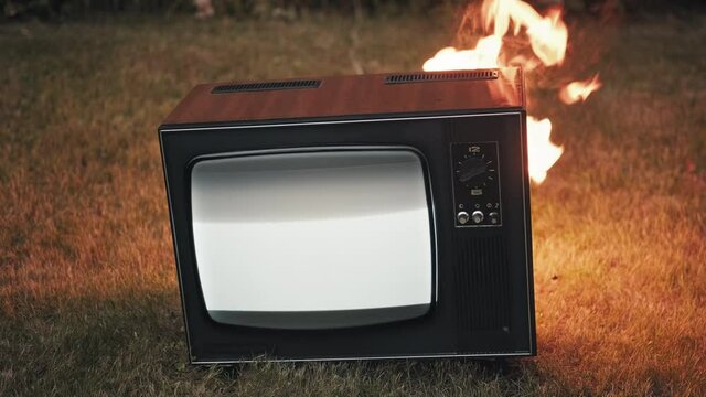Old vintage retro TV is standing on the street and is burning with fire. There is interference on the TV screen. Concept of the fire hazard of old worn out equipment
