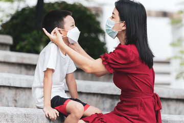 Mom is wearing a medical mask for her child. Little asian boy and mom in medical mask. Asian family protection virus concept.