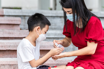 Mom and son wearing a medical mask during coronavirus and flu outbreak. Little Asian boy and mom wash their hand with alcohol gel. Asian family protection virus concept.