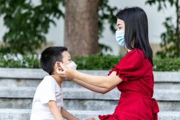 Mom is wearing a medical mask for her child. Little asian boy and mom in medical mask. Asian family protection virus concept.