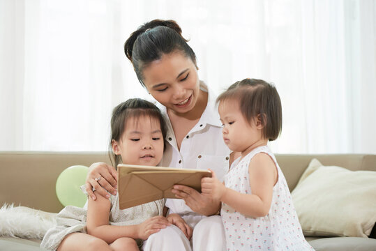 Smiling pretty young woman showing educational animated cartoon to her two little children