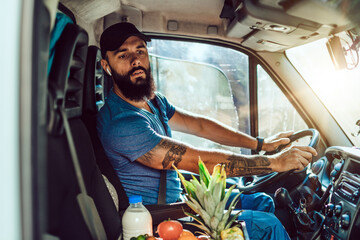 Young bearded man is driving delivery van. He is working in everyday or daily home delivery service.