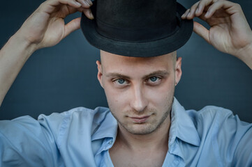 portrait of a young man holding his hat off his head with his hands showing his baldness