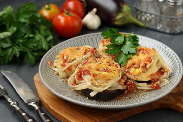 Spaghetti with eggplants, tomatoes, garlic and cheese on a gray plate on a wooden board. Vegetarian food