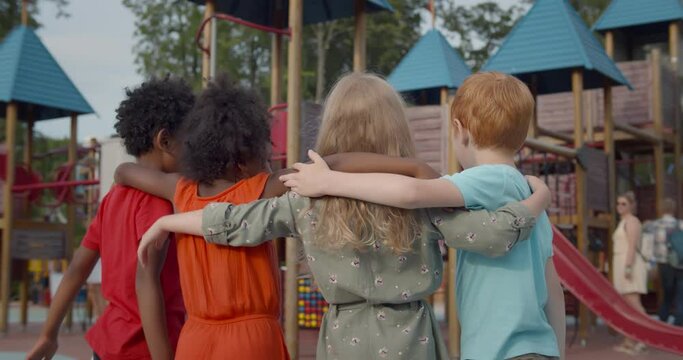 Back view of diverse preschool kids embrace on playground