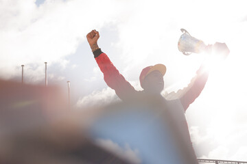 Cheering racer holding trophy on track - obrazy, fototapety, plakaty