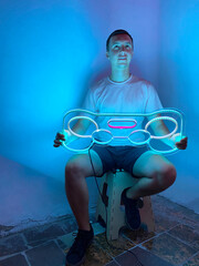 Fototapeta na wymiar A man is holding a neon joystick sign in pink, blue and white color. Trendy style. Neon sign. Custom neon. Summer vibe. Play game.