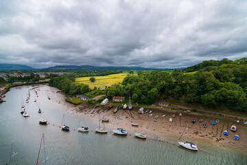 top view of boats lined up in a canal, next to a meadow, under a cloudy sky, beside Caernarfon Castle.