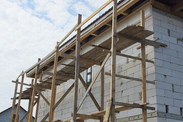 unfinished house with gray wooden repair boards and a white brick wall in the street