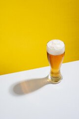 Cold beer served in a glass with white foam on a white table and yellow background